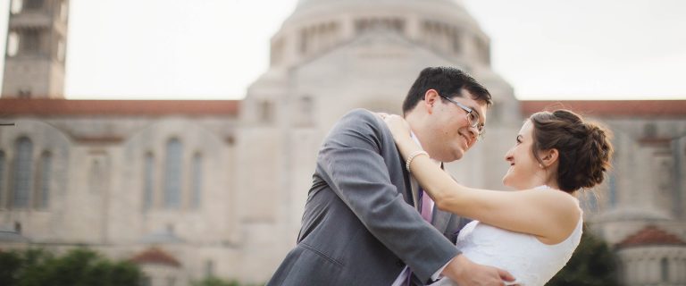 A bride and groom hugging in front of a Catholic church in Washington DC.