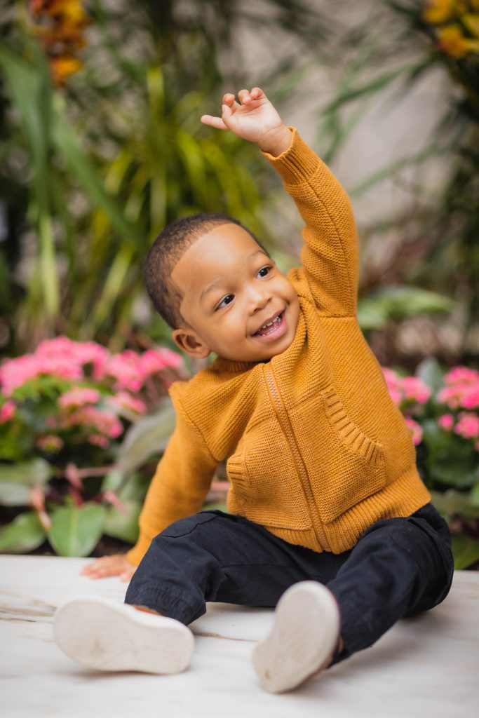 A baby boy in a yellow sweater is sitting on the ground at the National Portraits Gallery.