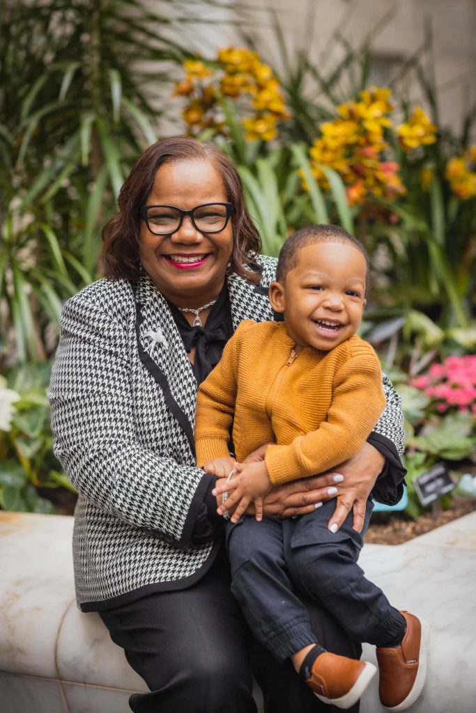 An African-American woman holding a child in front of flowers at the National Portraits Gallery, capturing a touching family moment.