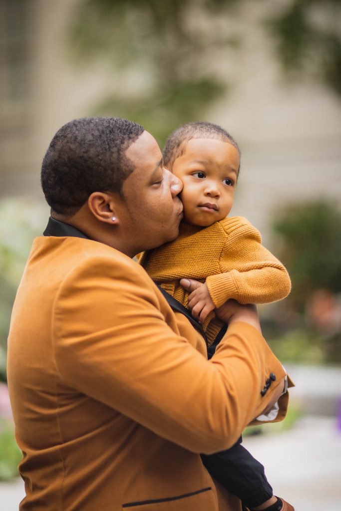 A family poses for a portrait in front of the National Portraits Gallery as a man affectionately kisses his son.