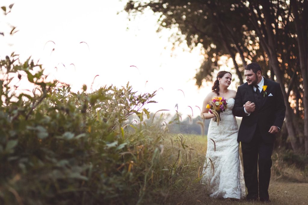 A bride and groom walking through tall grass at Kent Island Resort during sunset.