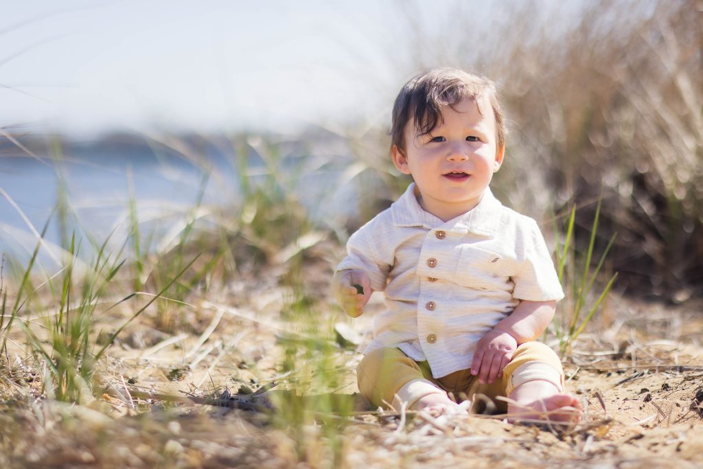 A family portrait with a baby sitting in the grass near a body of water at Annapolis.