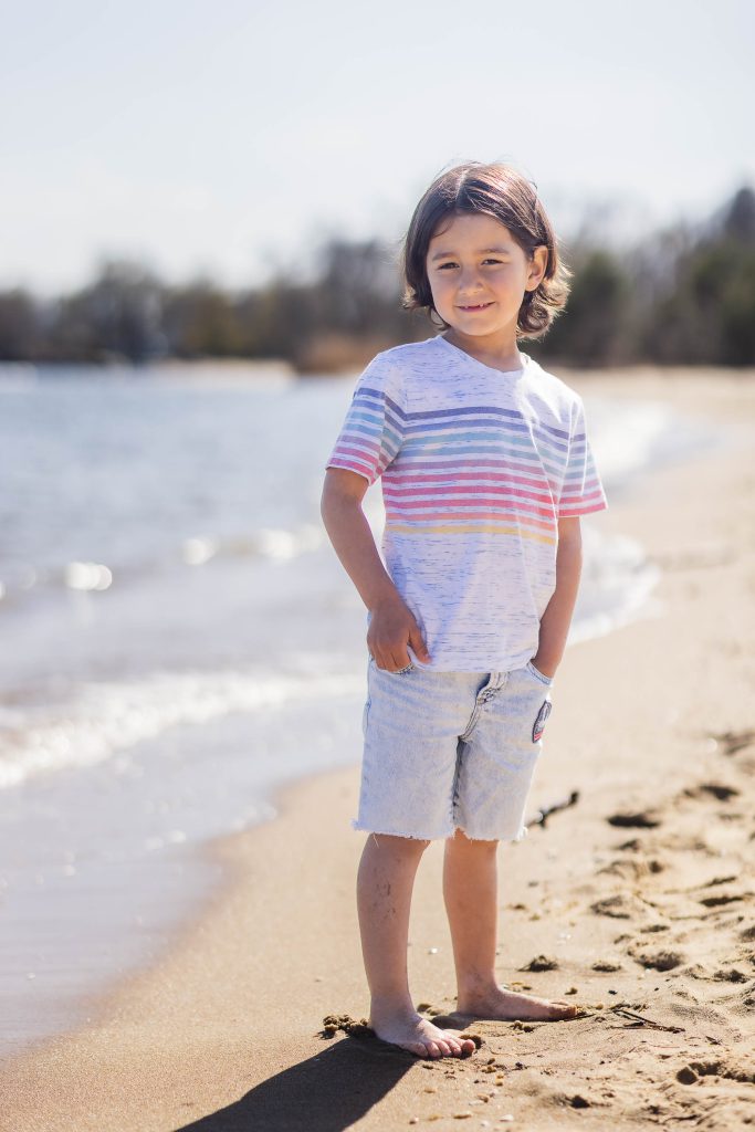 A young boy standing on the beach wearing a striped t-shirt in Maryland.