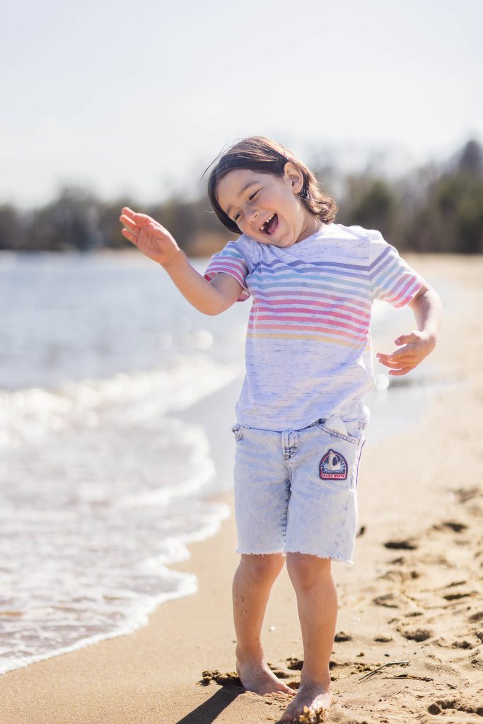 A little girl is standing on the beach with her arms out, capturing a portrait in the serene landscape of Maryland's Chesapeake Bay Foundation.
