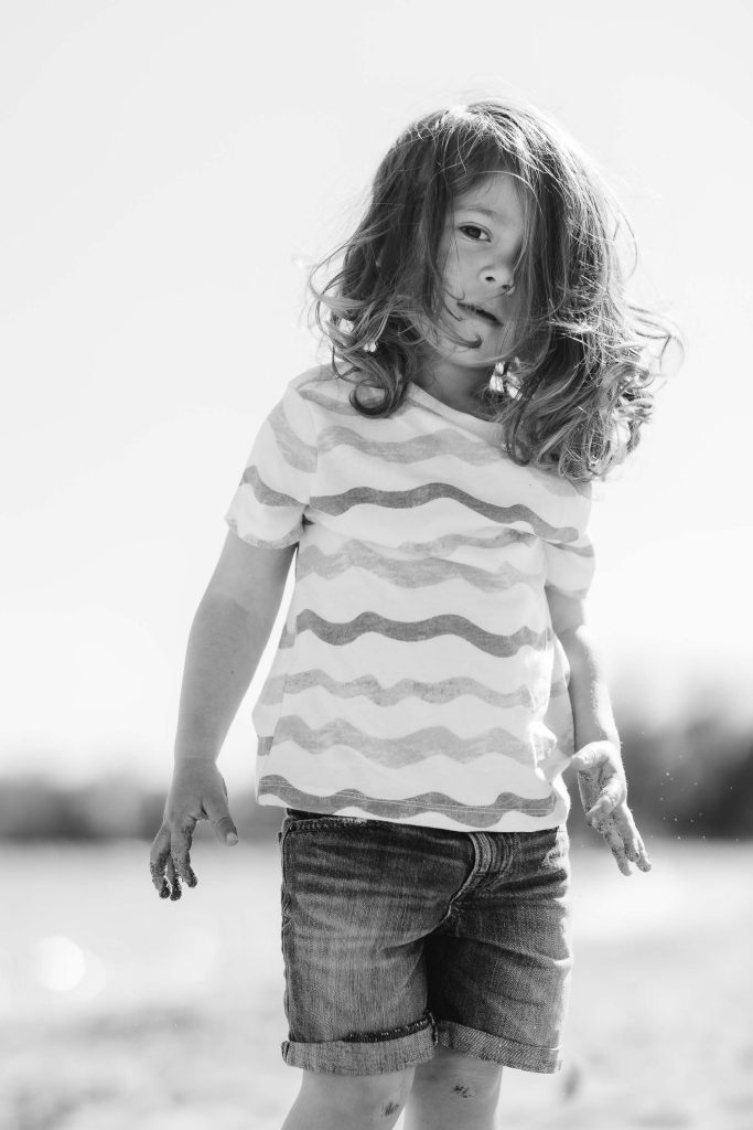 A black and white portrait of a little girl running on the beach.