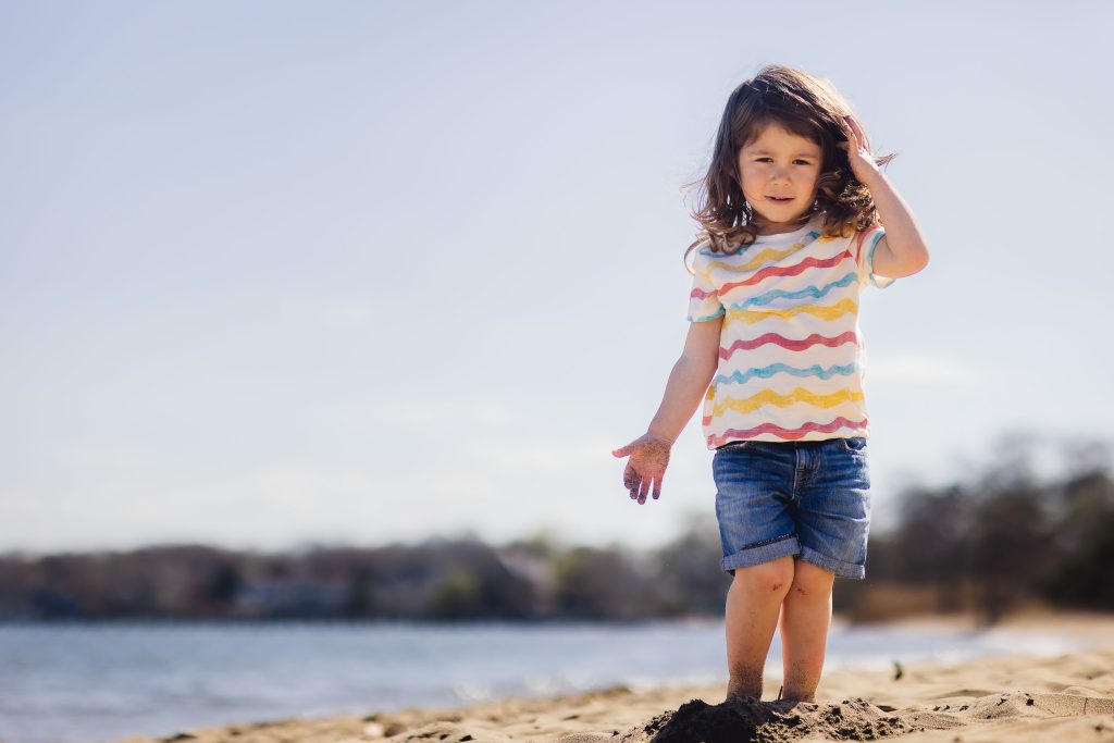 A family portrait taken in Annapolis, with a little girl standing in the sand on the beach.