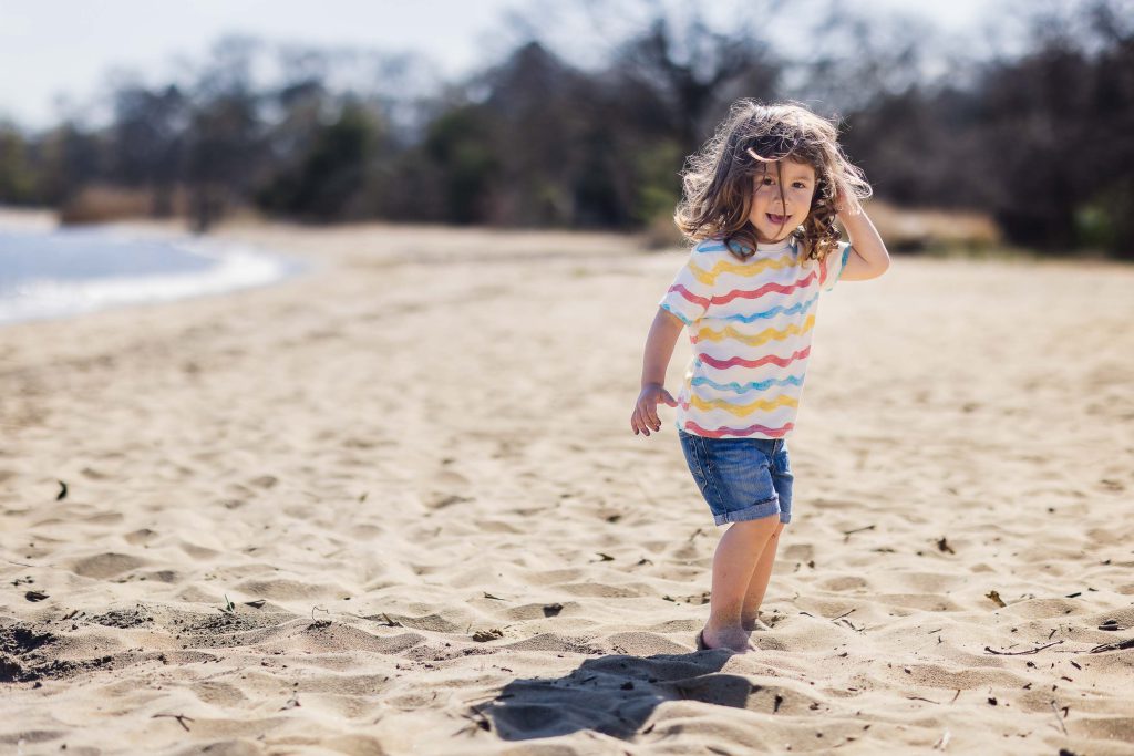 A little girl from a Maryland family walking on a sandy beach.