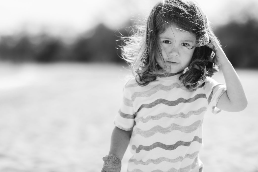 A black and white portrait of a little girl standing on the beach with her family in Maryland.
