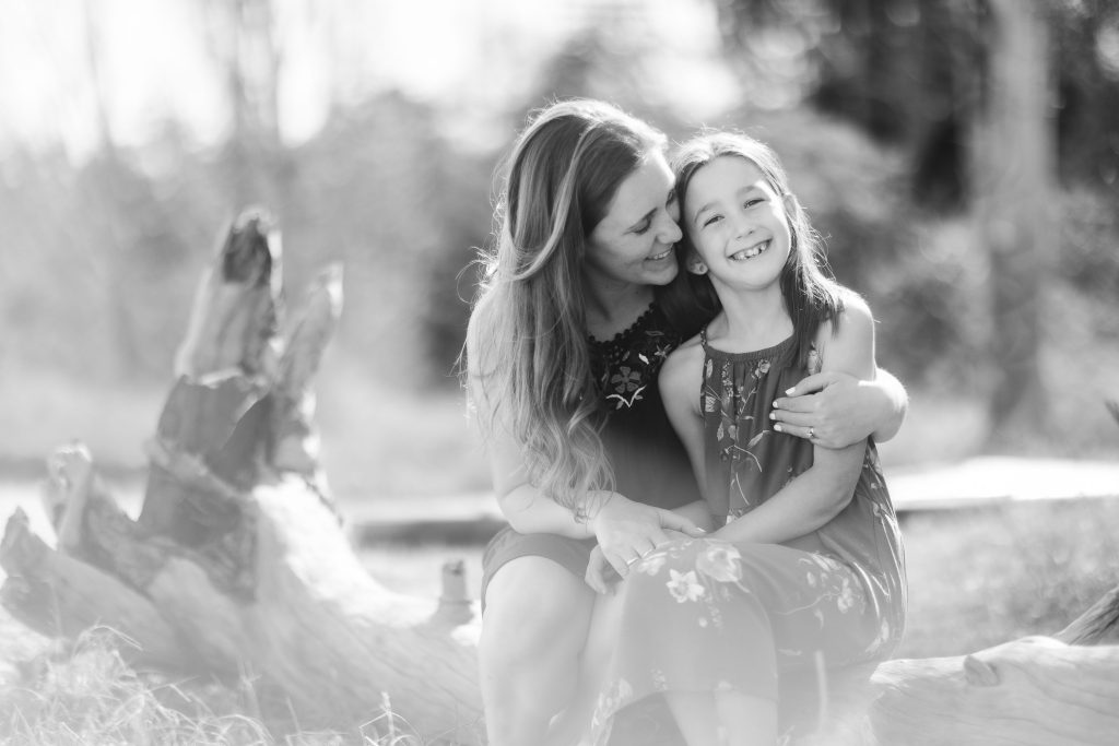 A black and white family portrait of a mother and daughter sitting on a log in Annapolis.