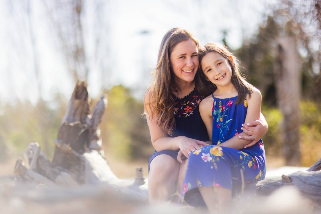 A mother and daughter sitting on a log in a field, captured in an Annapolis portrait.