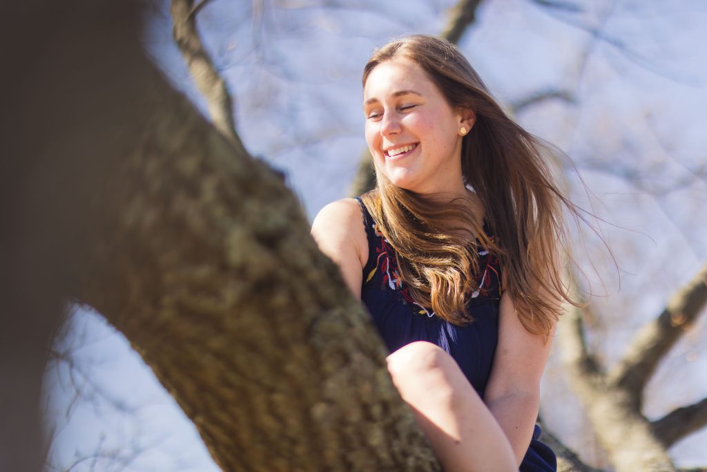A girl is sitting in a tree, capturing the perfect portrait moment.