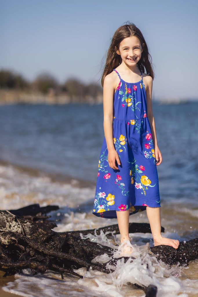 A portrait of a little girl in a blue dress standing on a log in Annapolis, Maryland.