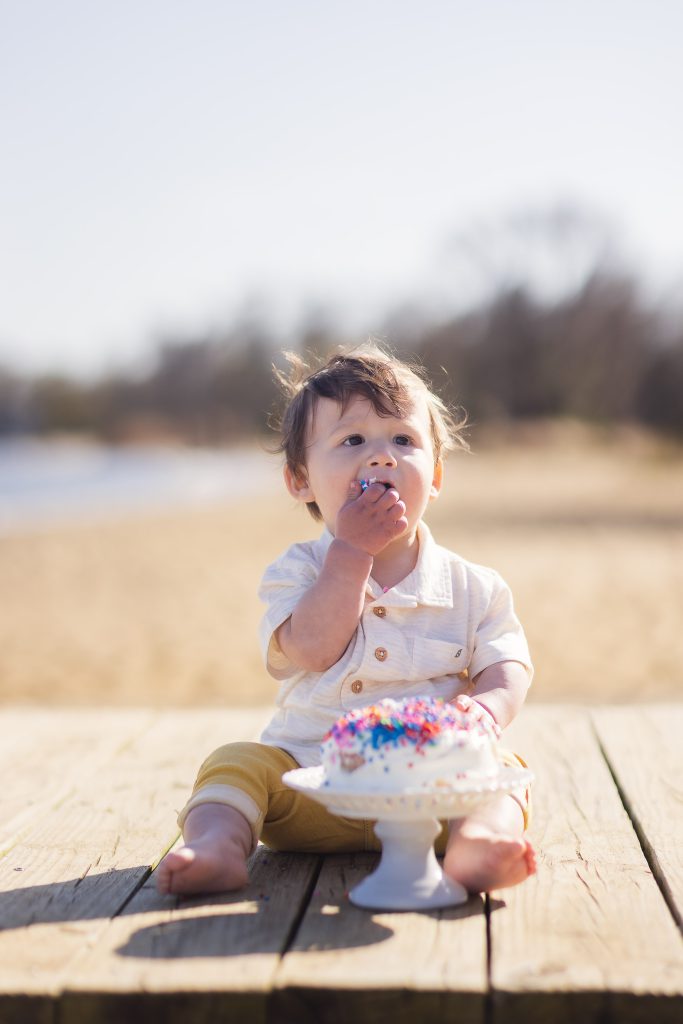 A baby sitting on a dock in Annapolis, Maryland, eating a birthday cake.