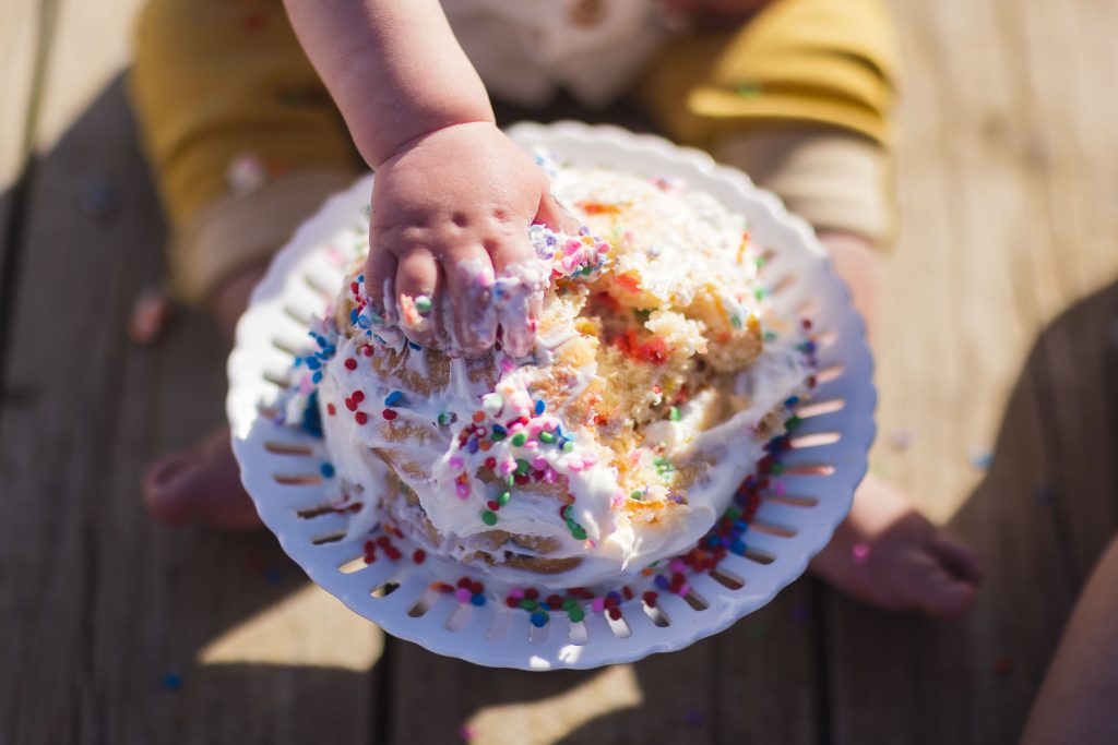 A child, surrounded by their loving family, is joyfully eating a cake topped with colorful sprinkles.