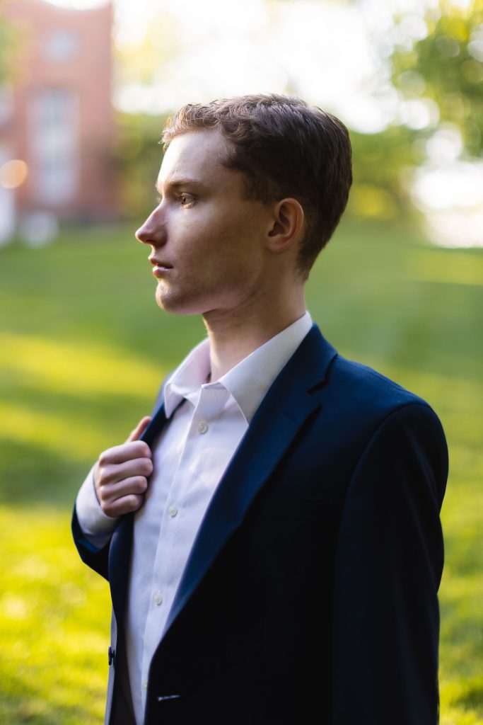 A High School Senior in a suit standing in a grassy area for his Graduation Portrait.