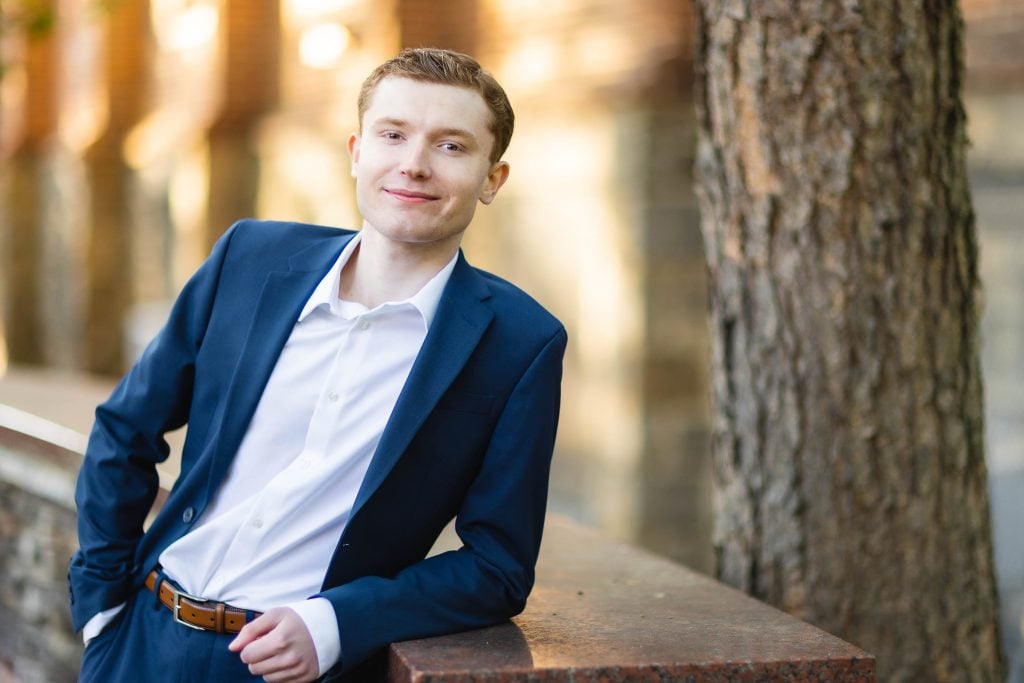 A High School Senior in a suit leaning against a wall in his Graduation Portrait.