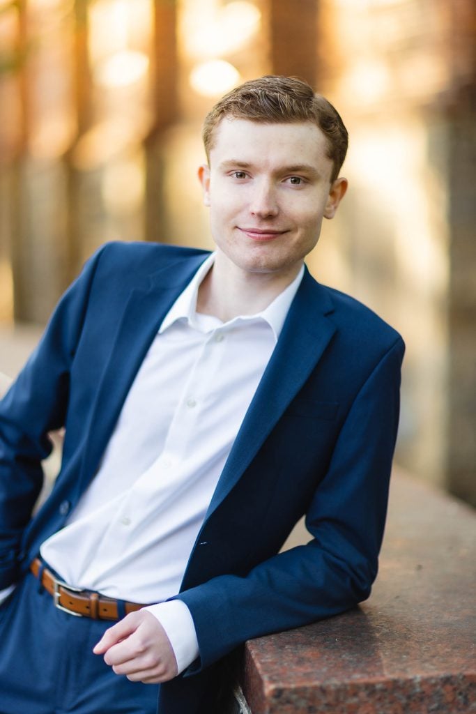 A young man in a blue suit leaning against a wall for his graduation portrait in downtown Annapolis.