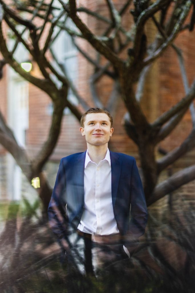 A High School Senior in a suit standing in front of a tree.