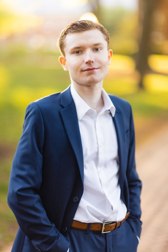 A high school senior in a blue suit standing in Downtown Annapolis park.