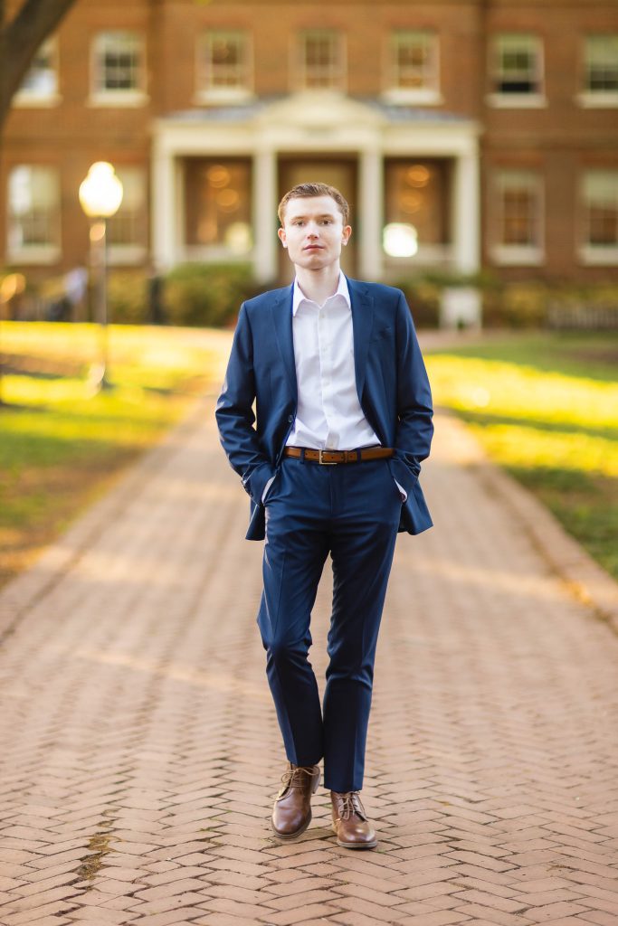 A young man in a blue suit, capturing his graduation portrait on a brick walkway in downtown Annapolis.