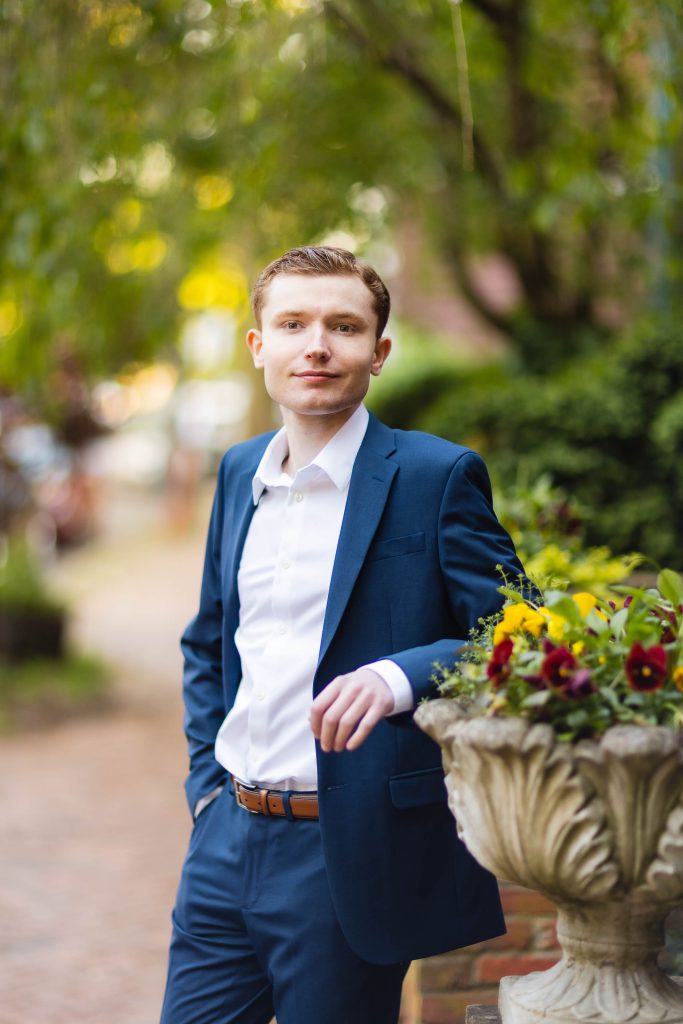 A high school senior in a blue suit leaning against a potted plant for his graduation portrait in downtown Annapolis.