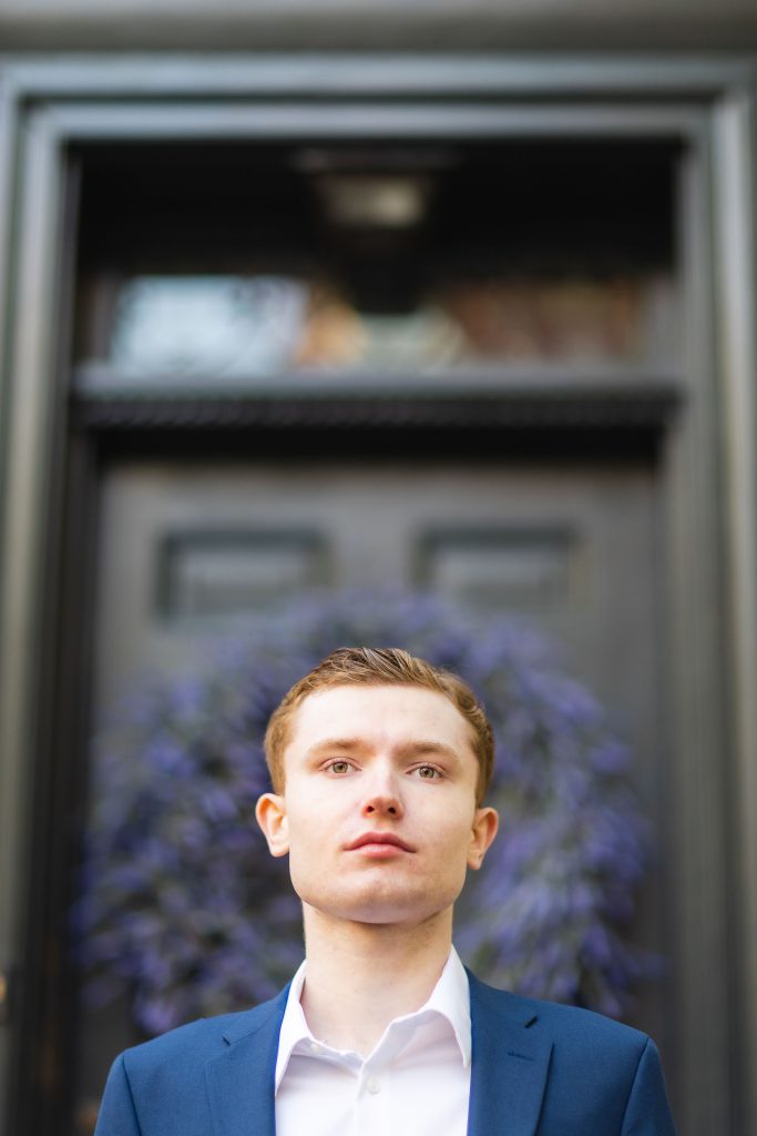 A High School Senior in a blue suit standing in front of a door for his Graduation Portrait in Downtown Annapolis.