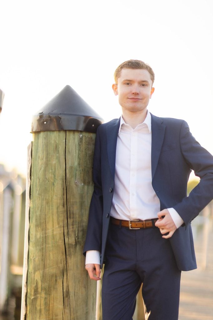 A High School Senior in a suit leaning against a wooden pole for their Graduation Portrait in Downtown Annapolis.