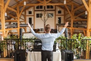 A District Remix dj in a barn with his hands up in the air.