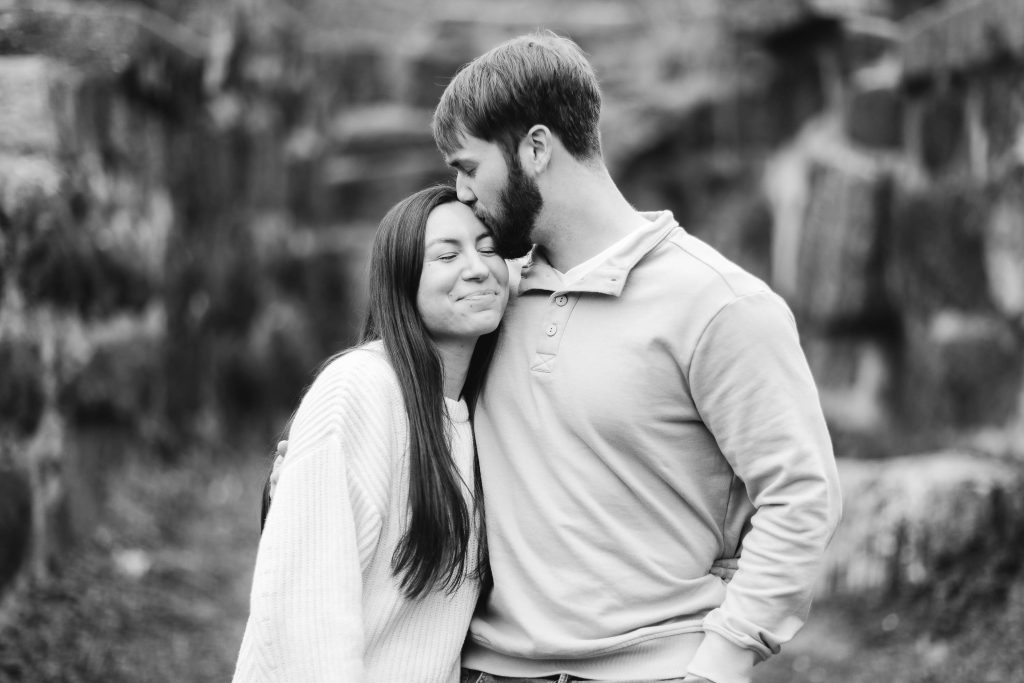 An engagement portrait of a couple embracing in front of a stone wall in Old Ellicott City.