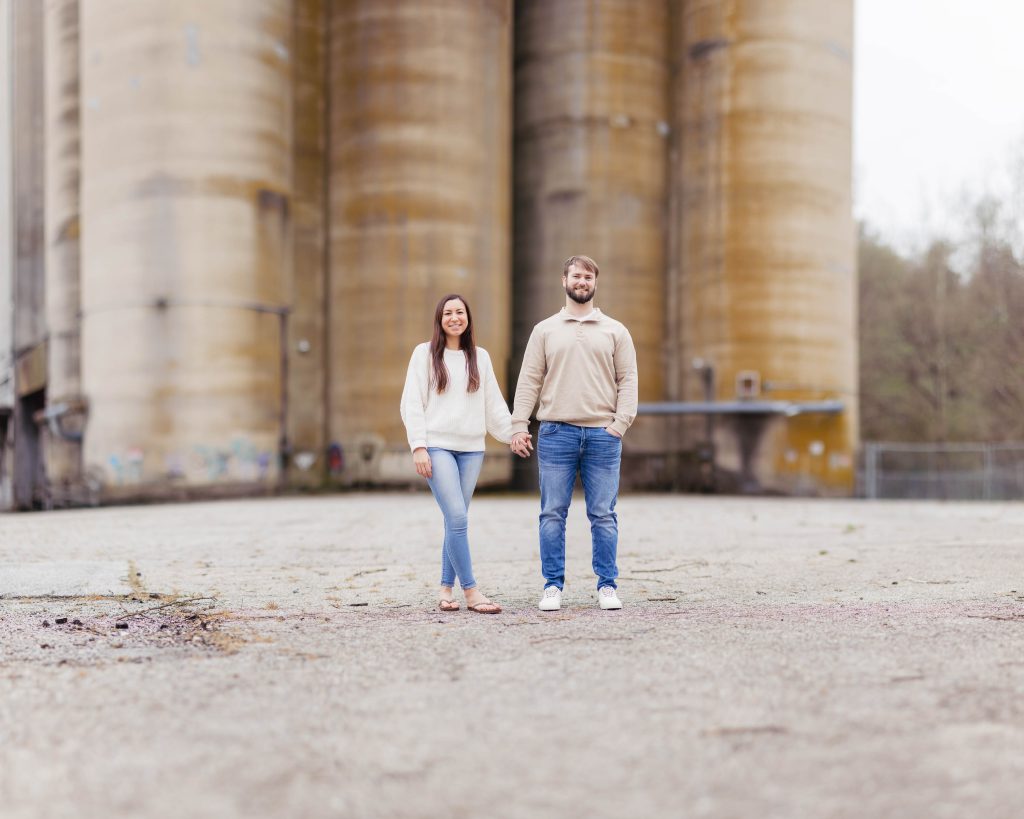 An engaged couple standing in front of a large silo, capturing their romantic portrait during an engagement photo session in Old Ellicott City.