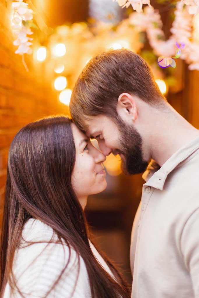 An engagement photo of a couple passionately kissing in front of a brick wall adorned with beautiful cherry blossoms.