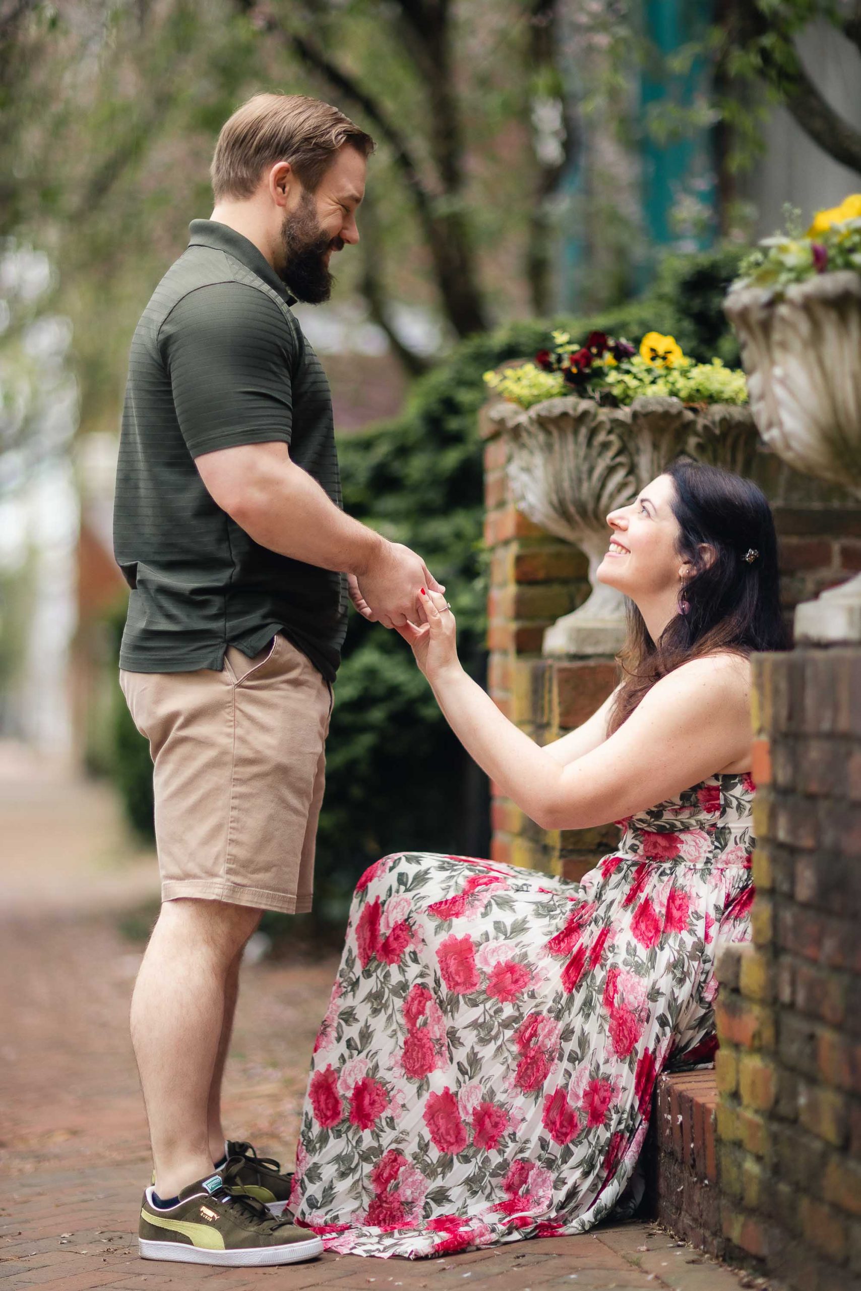 A couple is holding hands while sitting on a brick wall in downtown Annapolis, creating a picturesque scene for their engagement photos.