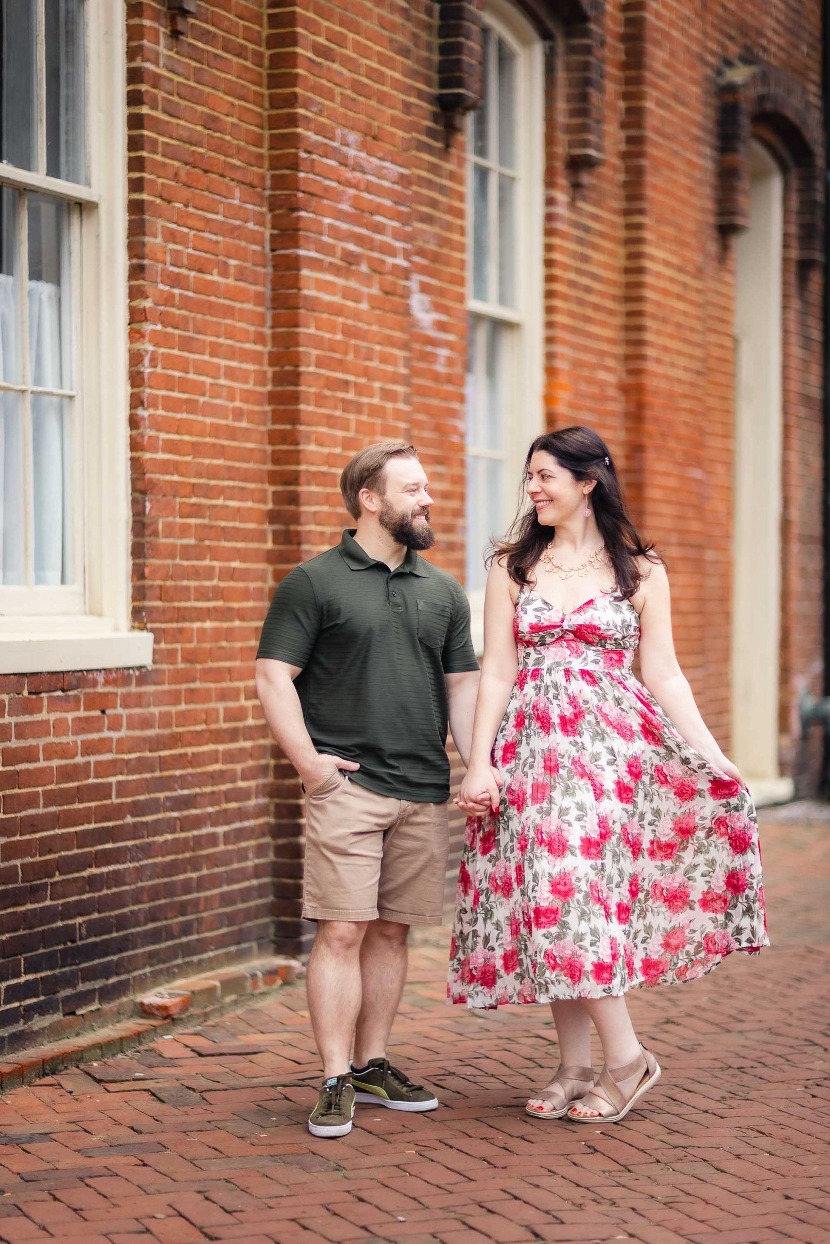 An engaged couple posing for their engagement photos in downtown Annapolis, in front of a brick building.