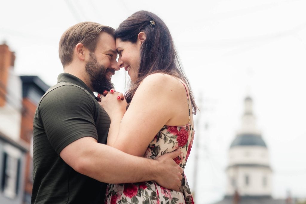 A couple embraces in front of a building with a clock tower in downtown Annapolis.