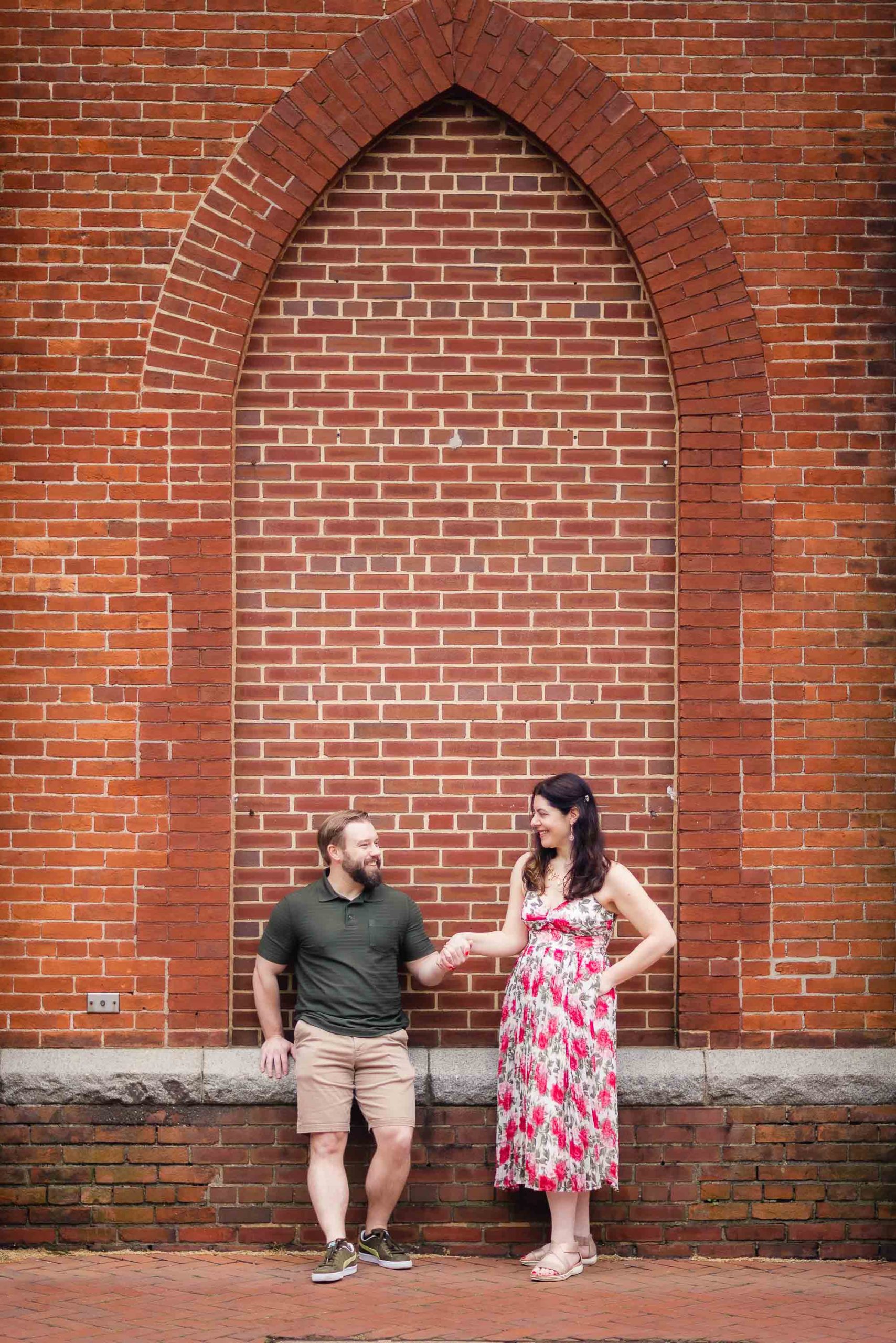 A portrait of an engaged couple standing in front of a brick wall in downtown Annapolis, capturing their beautiful engagement photos.