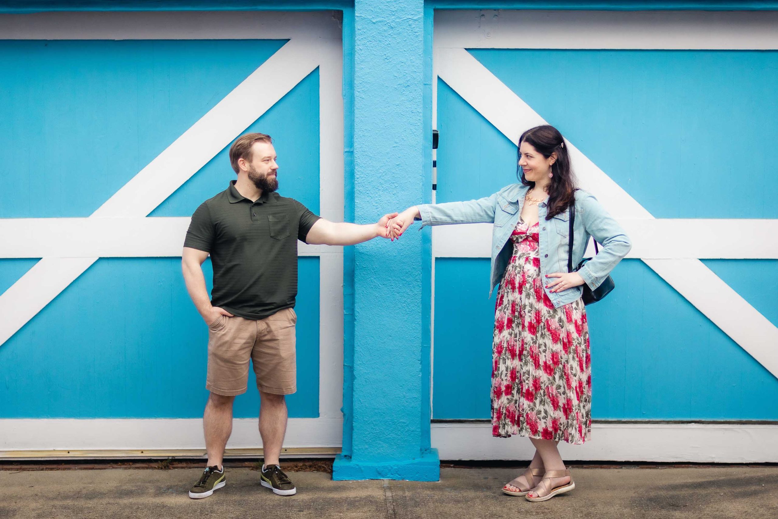 A man and woman, captured in a casual portrait, shake hands in front of a blue garage door.