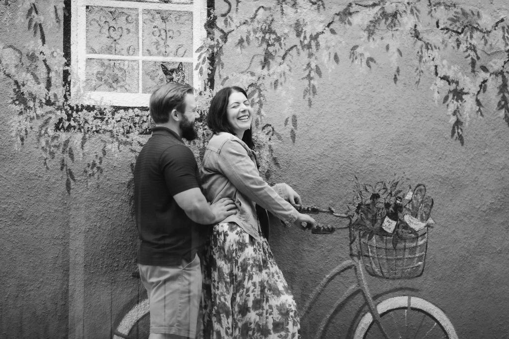 A black and white portrait of an engaged couple leaning against a downtown Annapolis wall with a bicycle in the background.