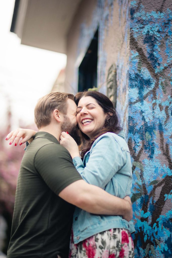 An engaged couple embraces in front of a painted wall, capturing a beautiful downtown Annapolis portrait.