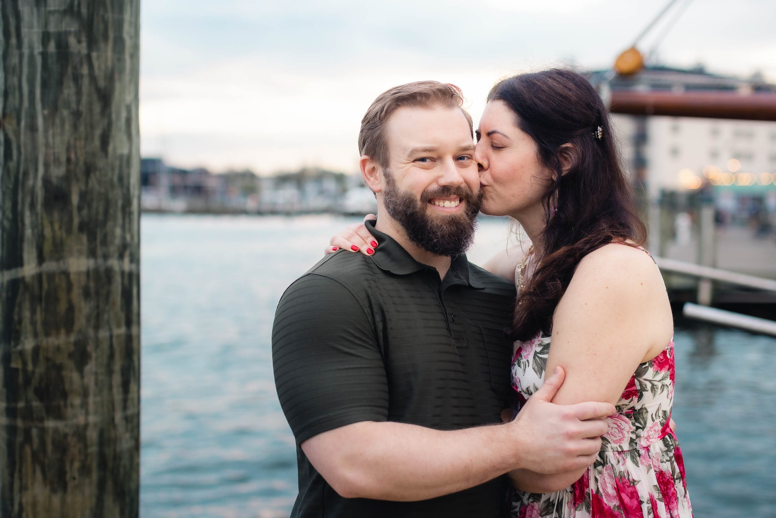 A couple shares a passionate kiss in front of a dock during their downtown Annapolis engagement photoshoot.
