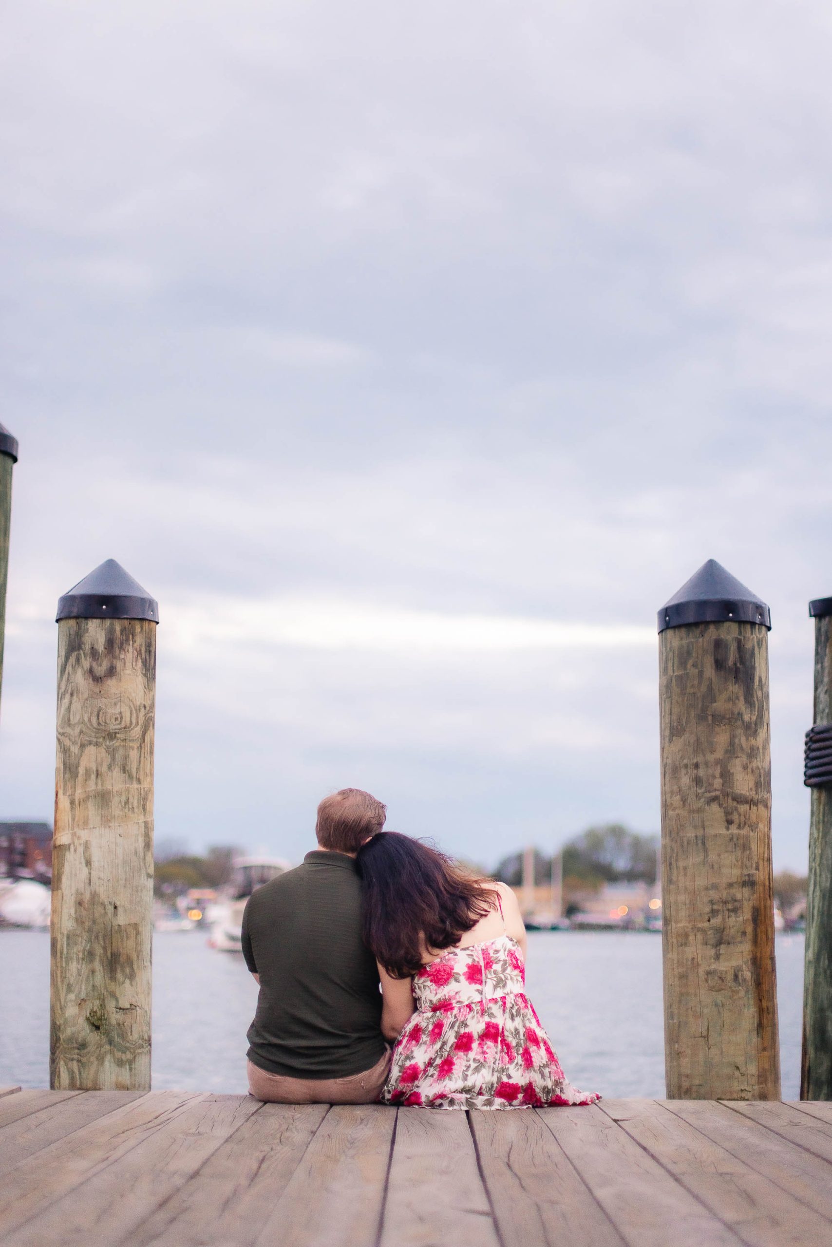 A couple sitting on a dock in downtown Annapolis, gazing at the water for their engagement photos.