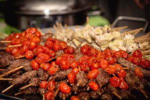 Event vendor offering skewers of meat and tomatoes on skewers.