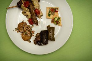 Event vendor offering a plate with a variety of food on it.