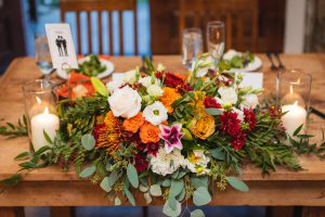 A rustic arrangement of flowers on a wooden table provided by an event vendor specializing in Vows & Vines.