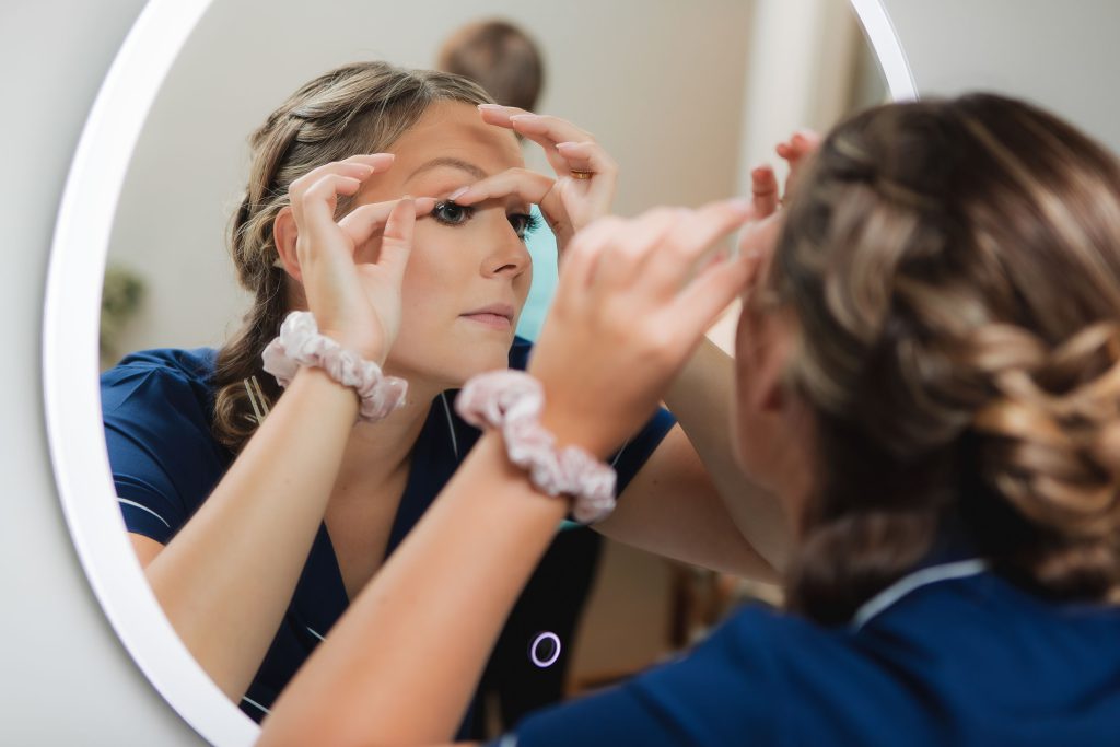 A candid bride getting her makeup done at Fleetwood Farm Winery for her wedding, in front of a mirror.