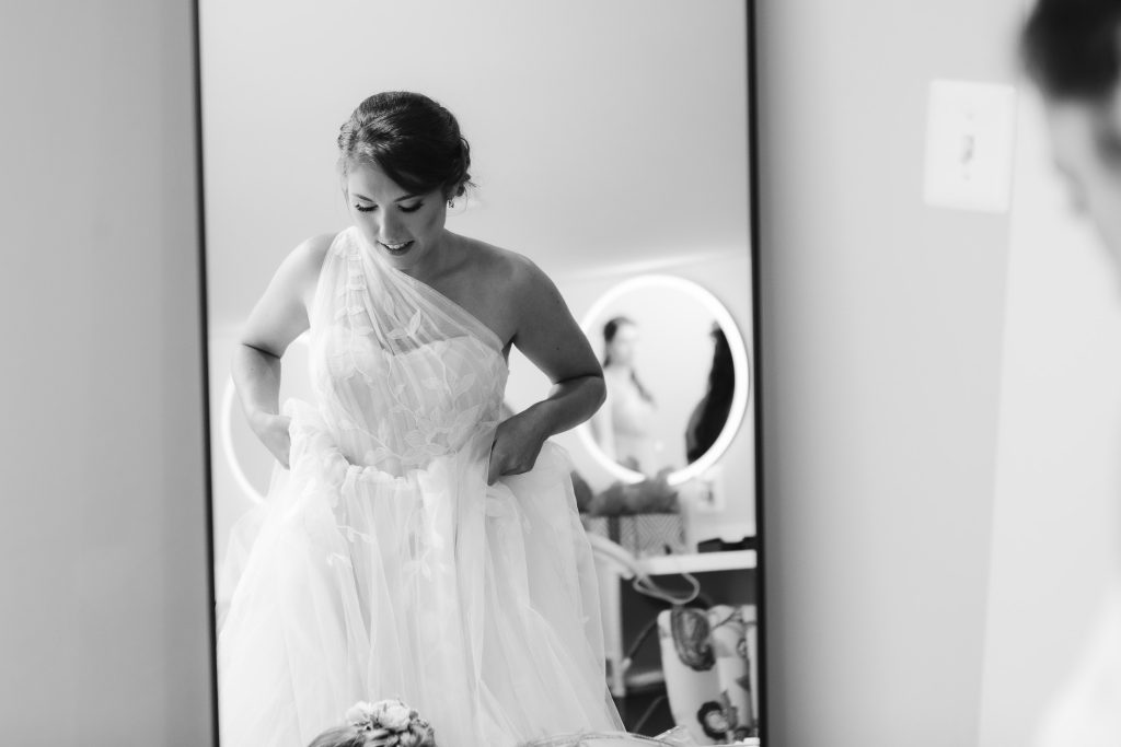 A candid bride at Fleetwood Farm Winery, putting on her wedding dress in front of a mirror.