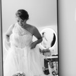 A candid bride at Fleetwood Farm Winery, putting on her wedding dress in front of a mirror.