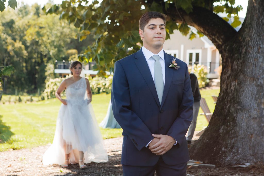 A candid wedding moment with the bride and groom standing in front of a tree at Fleetwood Farm Winery.