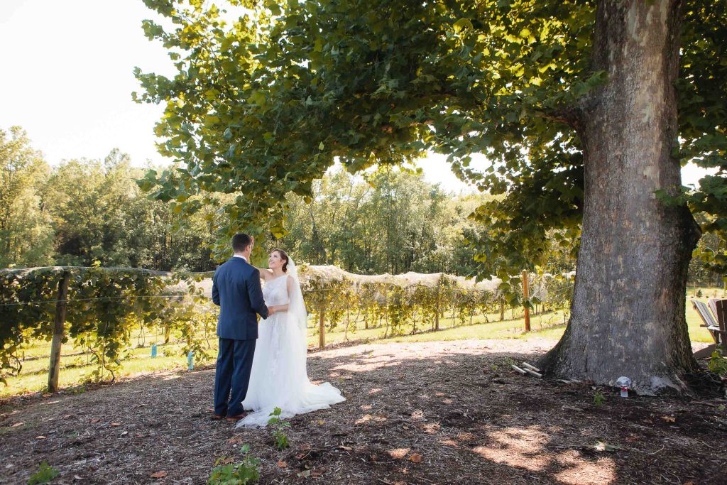A candid wedding shot of a bride and groom standing under a tree at Fleetwood Farm Winery.