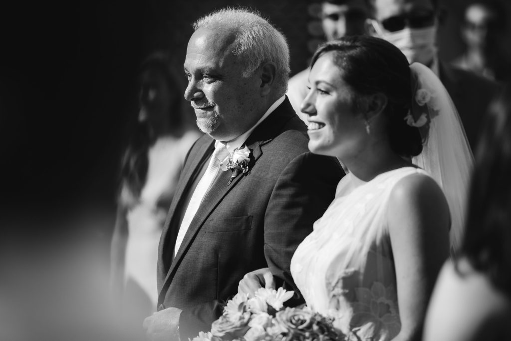 A black and white photo of a bride and her father walking down the aisle during their wedding ceremony at Fleetwood Farm Winery.