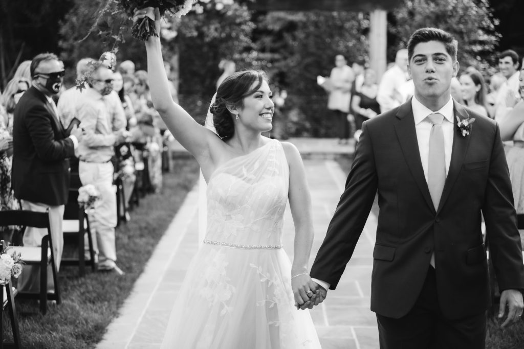 Black and white photo of bride and groom during their wedding ceremony at Fleetwood Farm Winery, walking down the aisle.